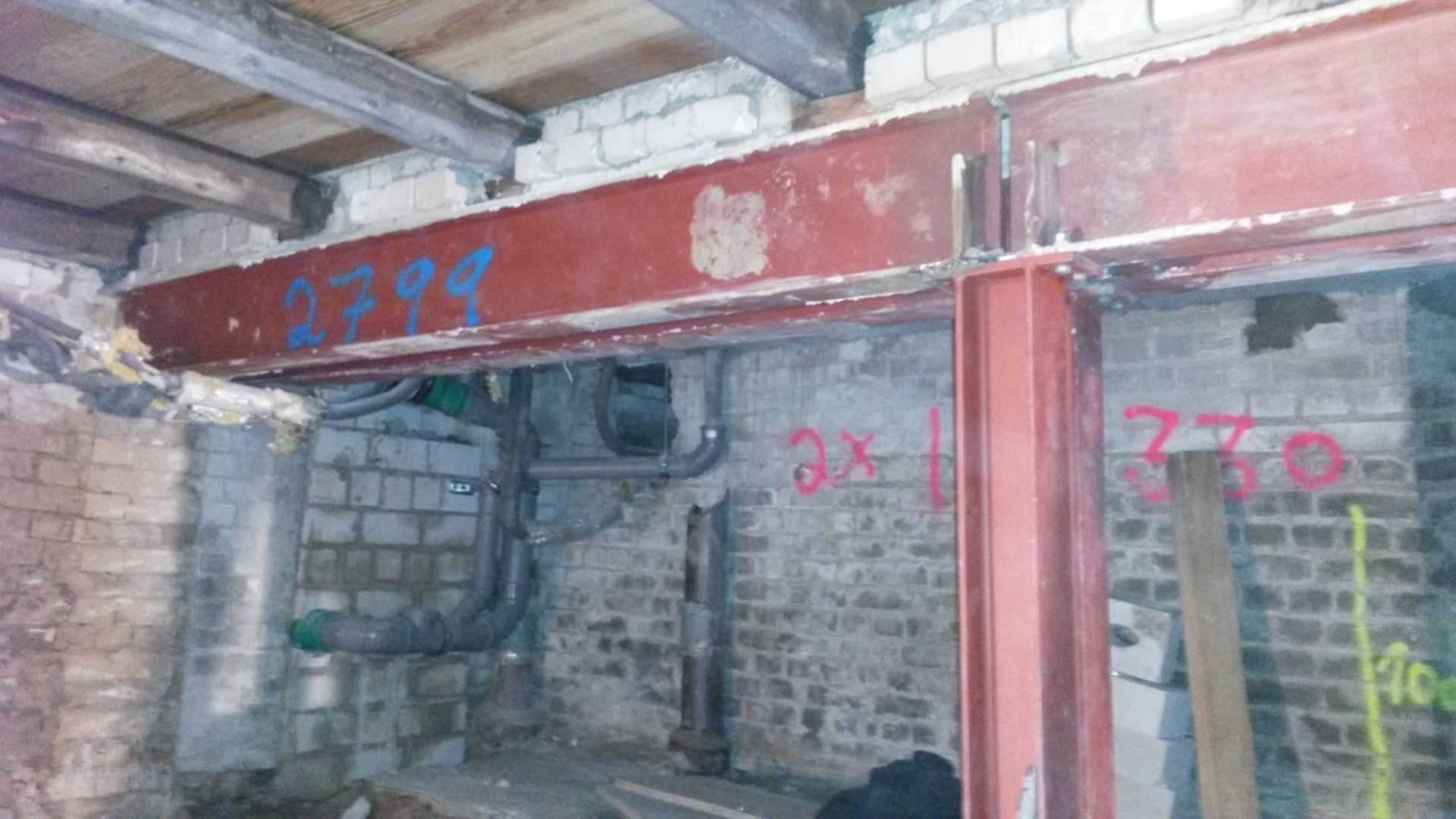 Beschädigter Innenraum mit freiliegenden Ziegelsteinen, roten Stahlträgern und Graffiti-Sprüchen an den Wänden.