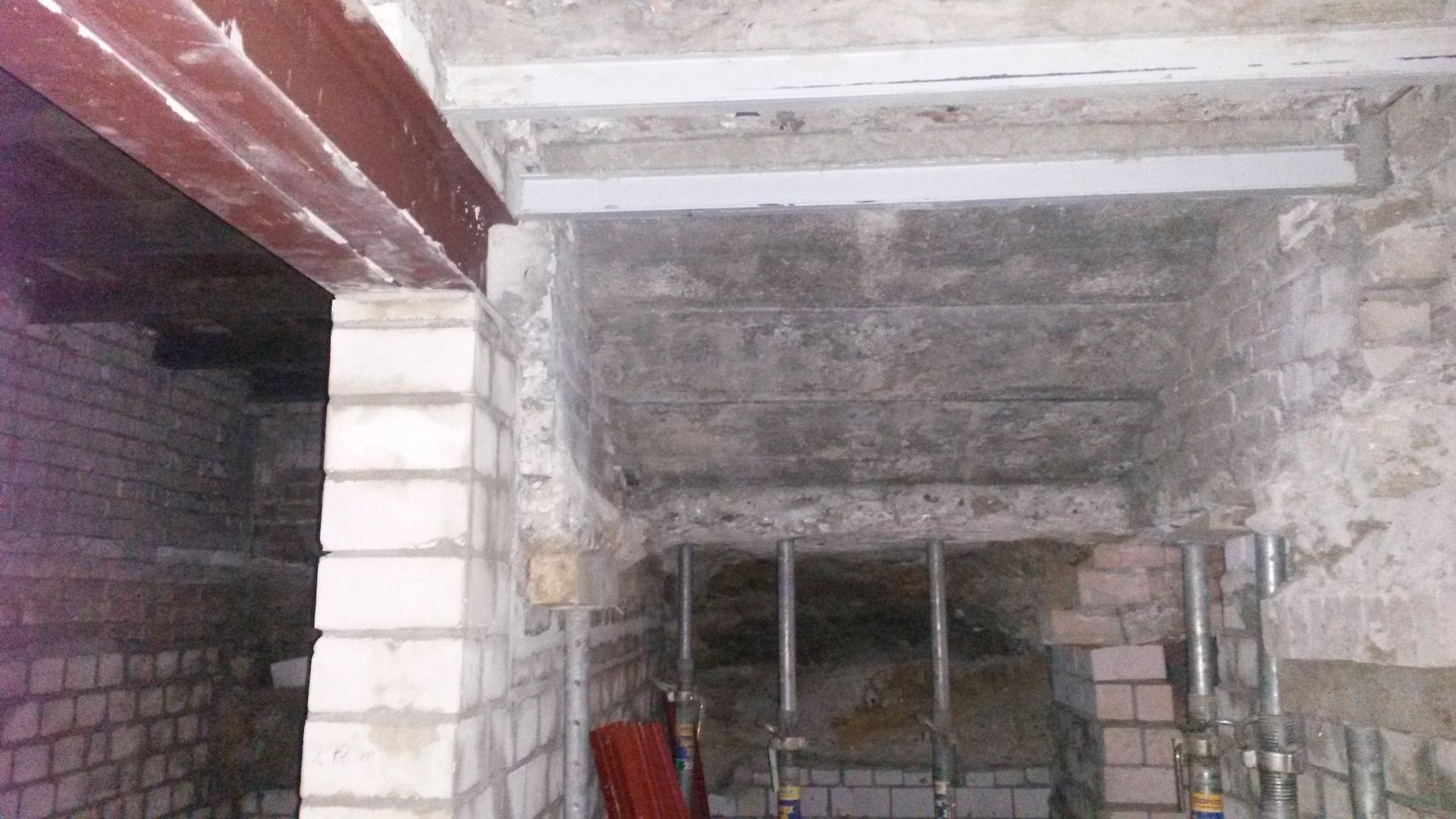 Dunkler, unfertiger Innenraum mit Betondecke, weißer Backsteinsäule und Baumaterialien.