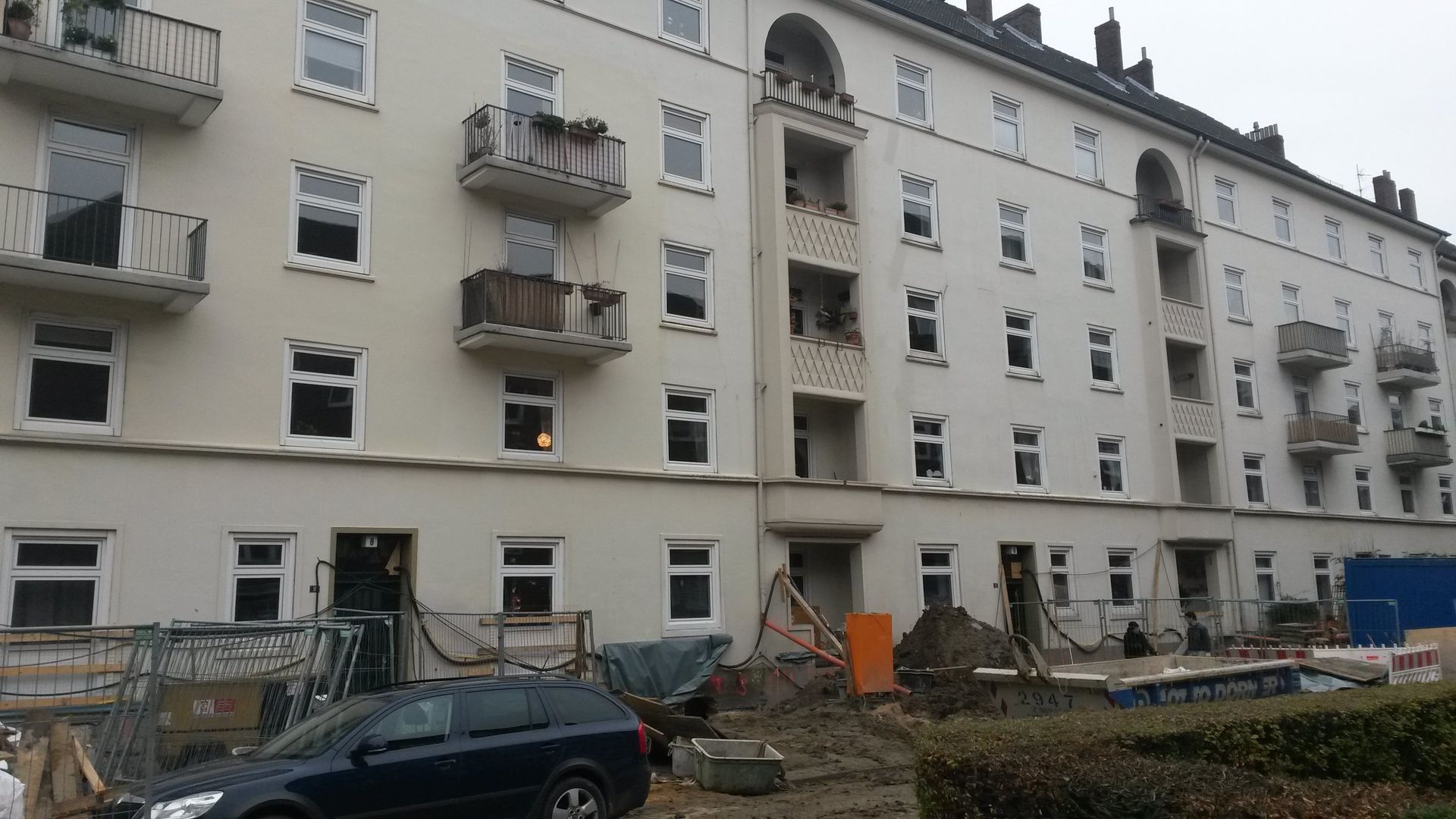 Beschädigtes Wohnhaus mit zerbrochenen Fenstern, Trümmern und einem davor geparkten Auto.