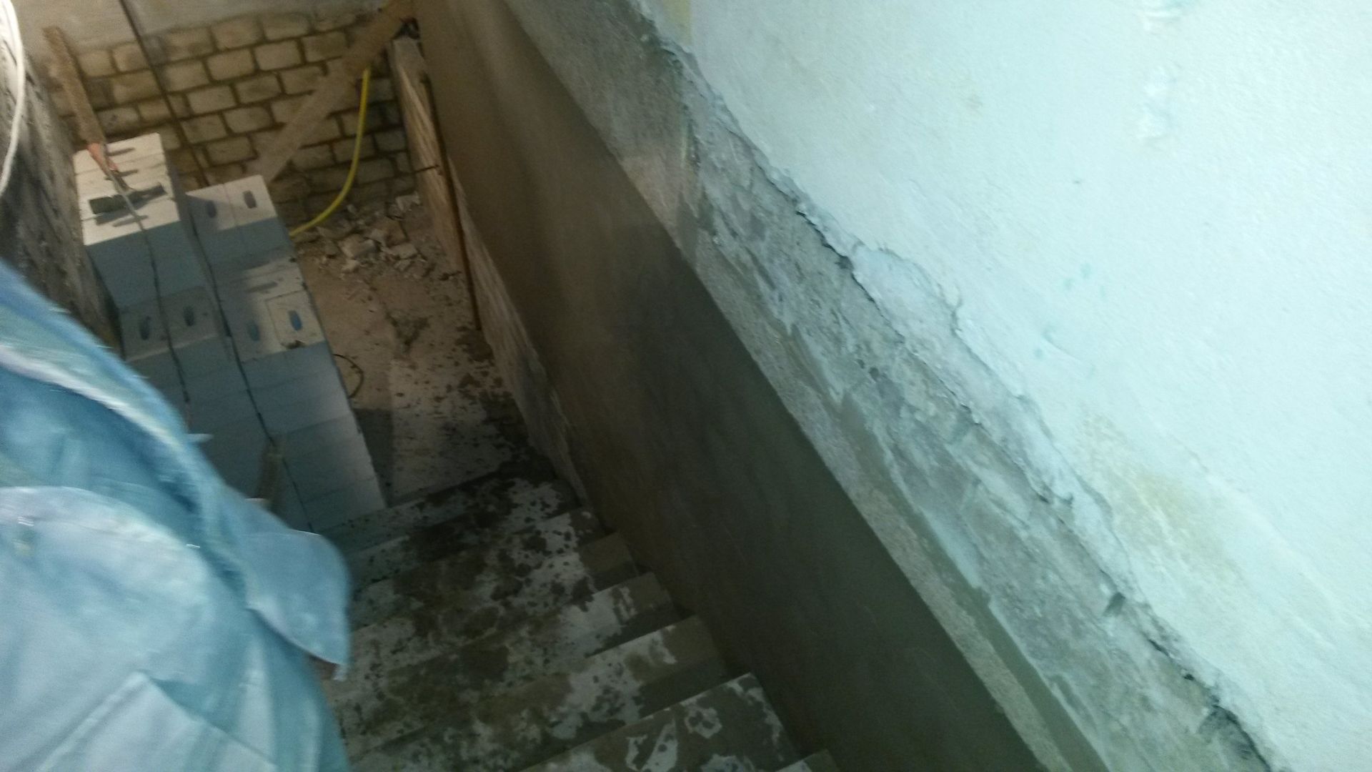 Ein schmales Treppenhaus neben einer Mauer, über dessen Stufen eine blaue Plane oder ein Tuch drapiert ist.