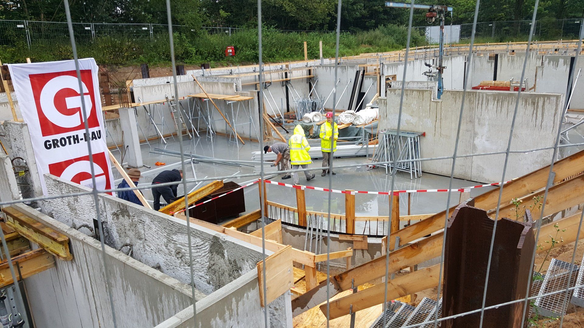 Baustelle mit Betonwänden, Arbeitern in gelben Westen und Holzschalung im Inneren eines Gebäudefundaments