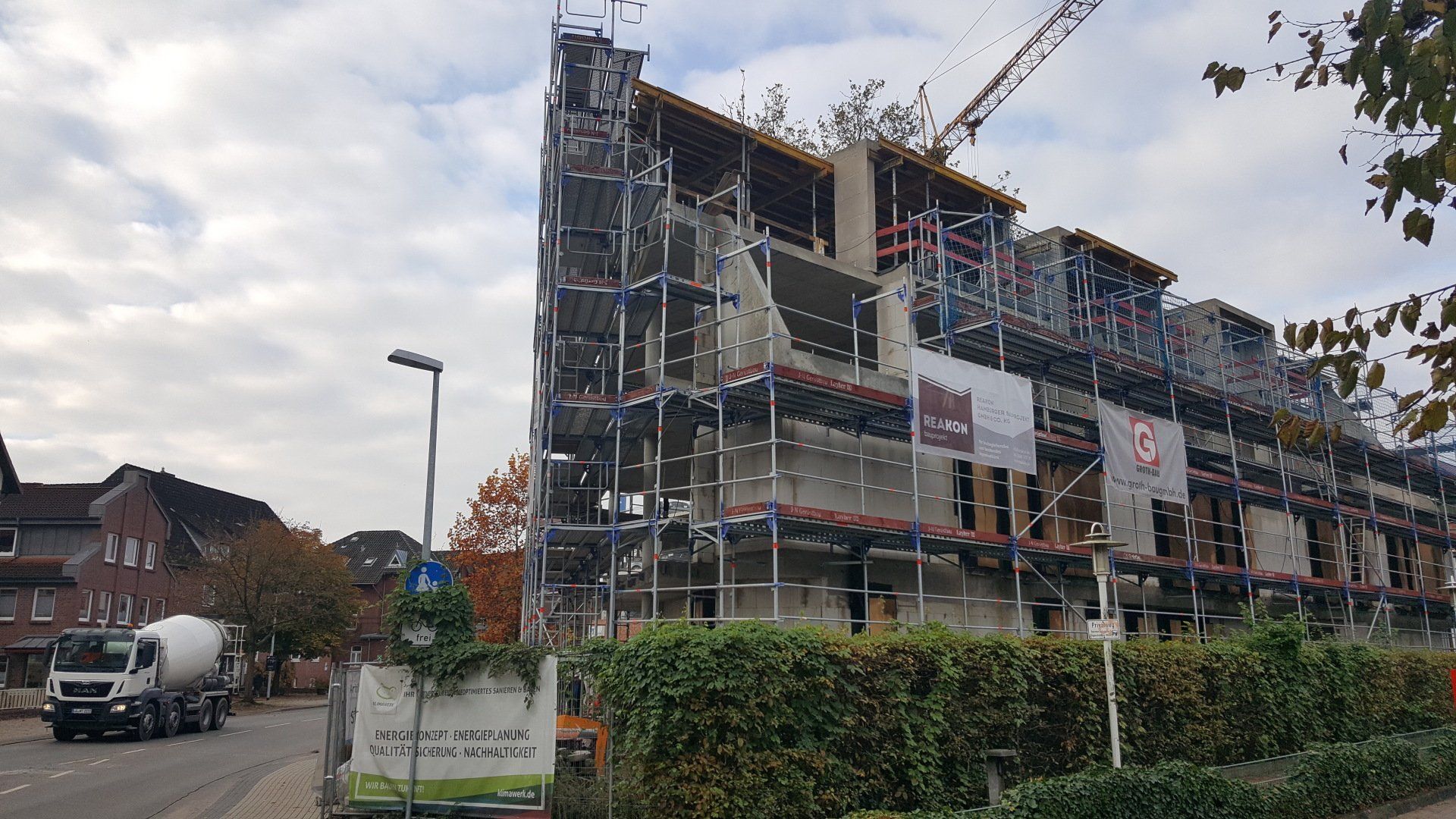Mehrstöckiges Gebäude im Bau mit Gerüst und Kran neben einer Straße und Hecken