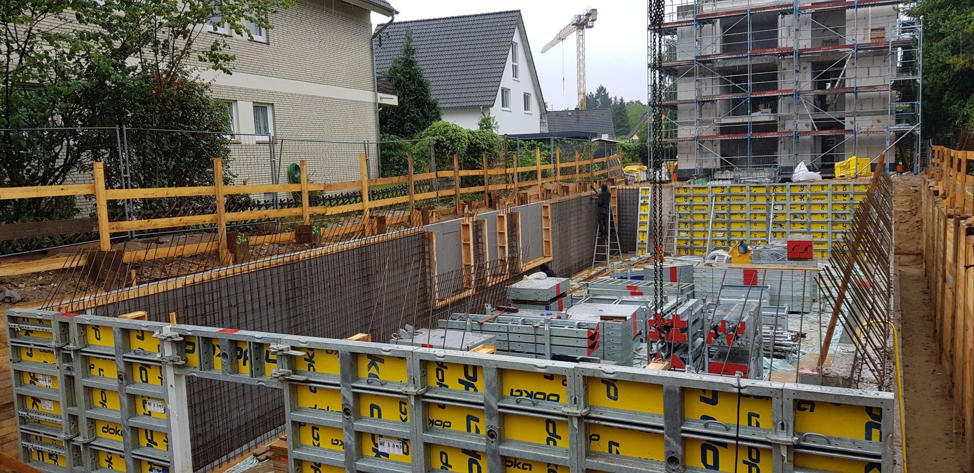 Baustelle mit Stahlbetonfundament, gelber Schalung, Gerüst und nahegelegenen Häusern
