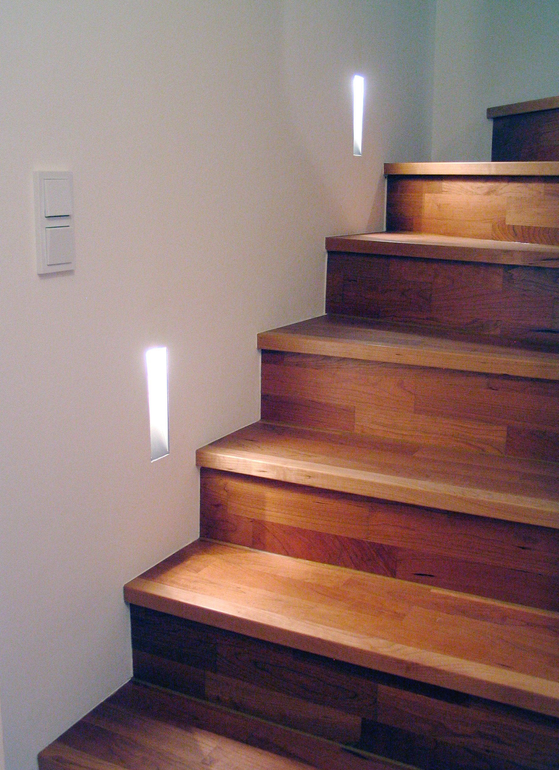Holztreppe mit eingebauten Wandleuchten entlang einer beigen Wand.