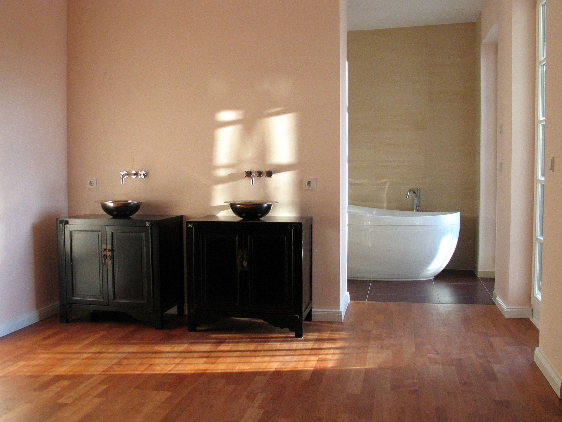Modernes Badezimmer mit zwei dunklen Waschtischen, Holzboden und einer weißen Badewanne in einer gefliesten Nische.
