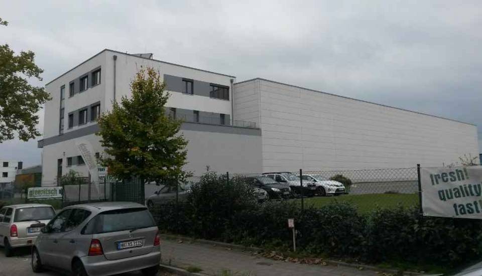 Modernes weißes Bürogebäude mit geparkten Autos und einer Hecke unter einem bewölkten Himmel