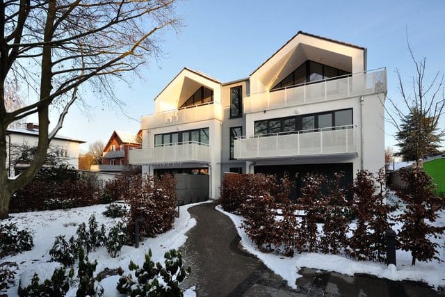 Modernes Haus mit schneebedecktem Garten und Bäumen im Winter