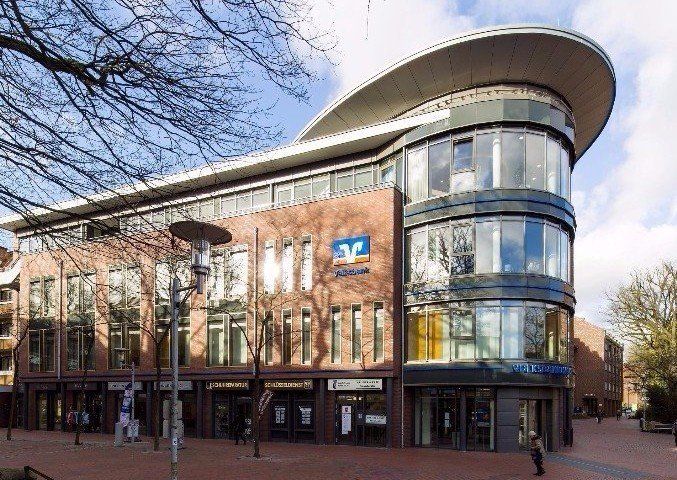 Modernes Backstein- und Glasgebäude mit geschwungenem Dach und großen Fenstern an einer Stadtstraße