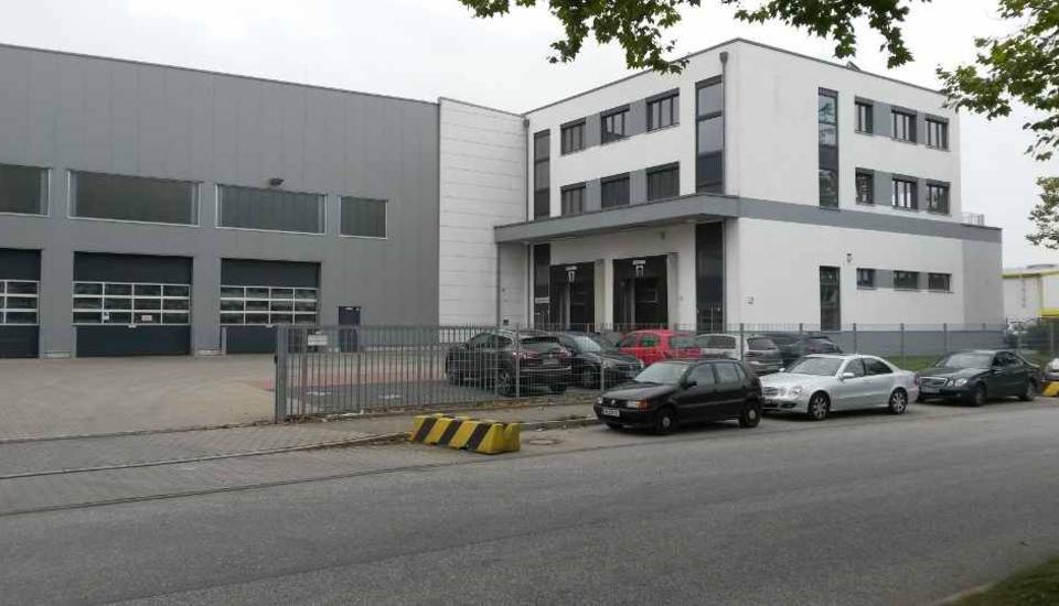 Modernes Industriegebäude mit geparkten Autos und einem umzäunten Gelände an einem bewölkten Tag