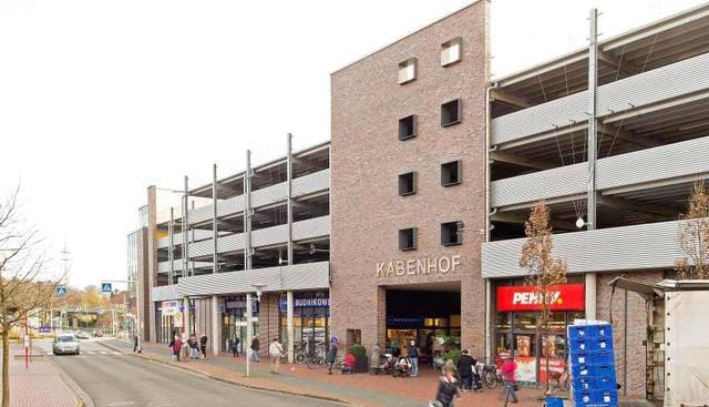Straßenansicht eines gemauerten Parkhauses mit Geschäften im Erdgeschoss und davor geparkten Fahrrädern.
