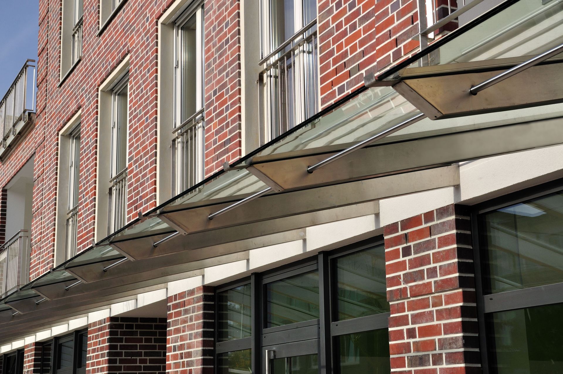 Backsteinfassade mit Fensterreihen und Metallmarkisen über einem Bürgersteigeingang