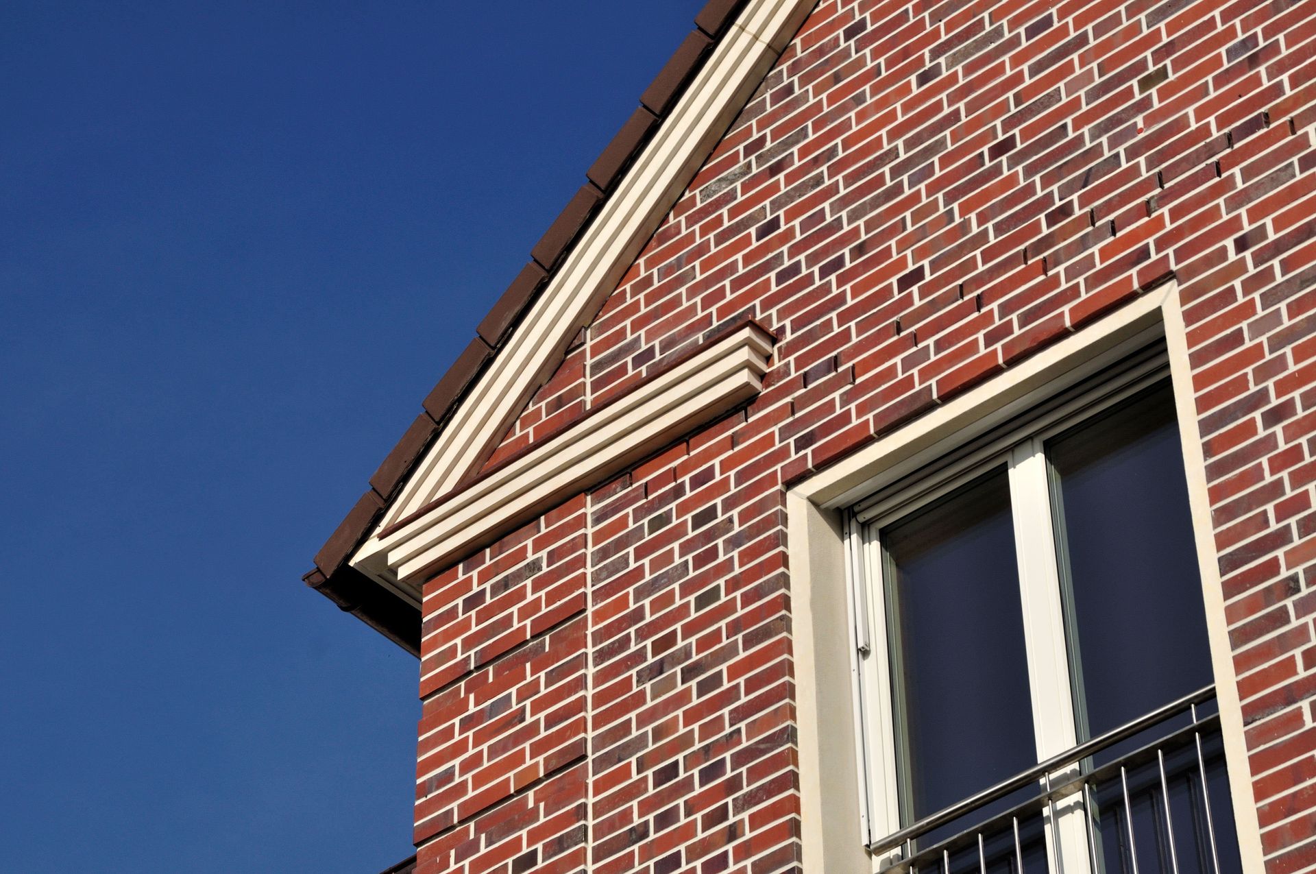 Ecke eines Backsteinhauses mit weiß umrandetem Fenster und blauem Himmel im Hintergrund