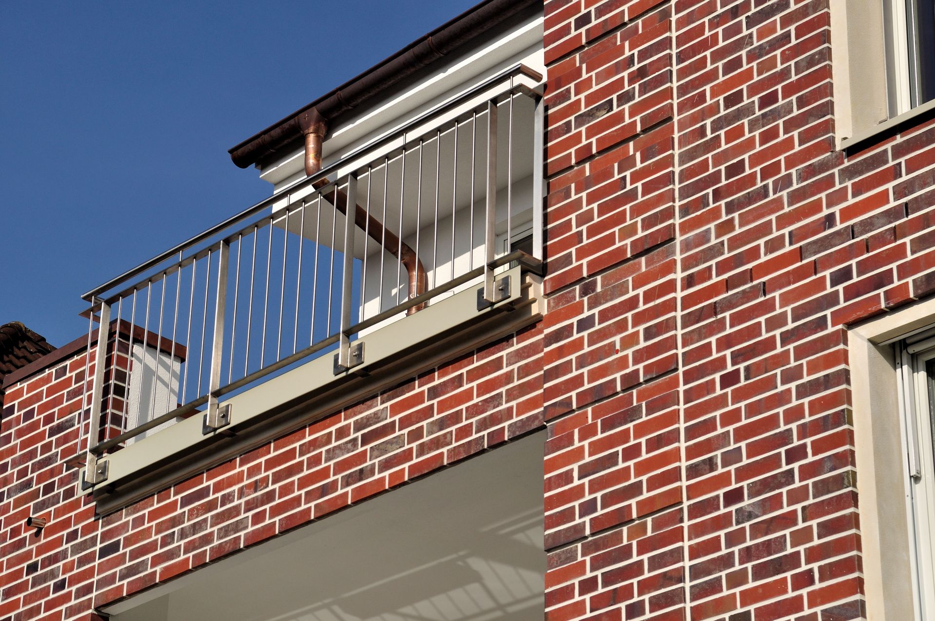 Ein rotes Backstein-Wohnhaus mit kleinem Balkon und blauem Geländer vor klarem Himmel