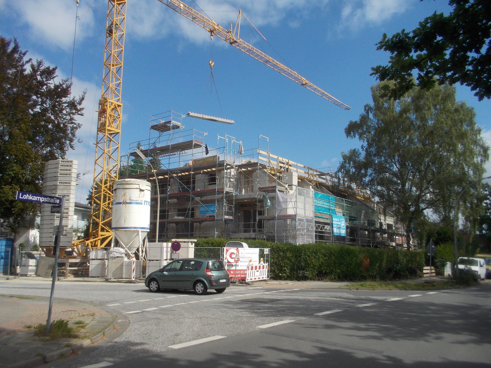 Baustelle mit Kränen und einem teilweise errichteten Gebäude neben einer Straße.