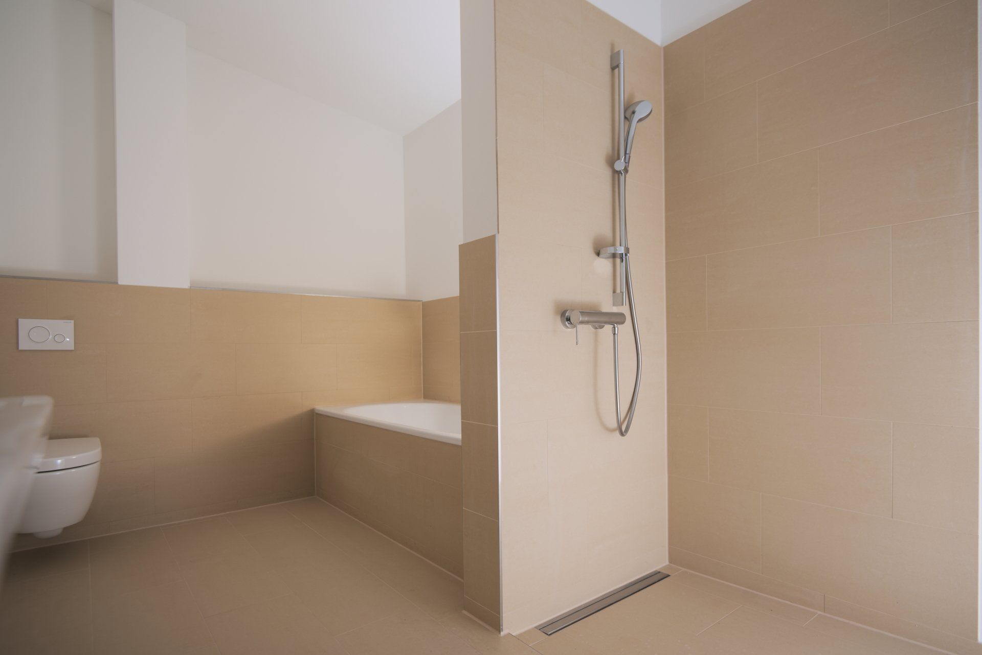 Barrierefreies Badezimmer mit Dusche, eingebauter Sitzbank und WC in beigefarbenen Fliesen.