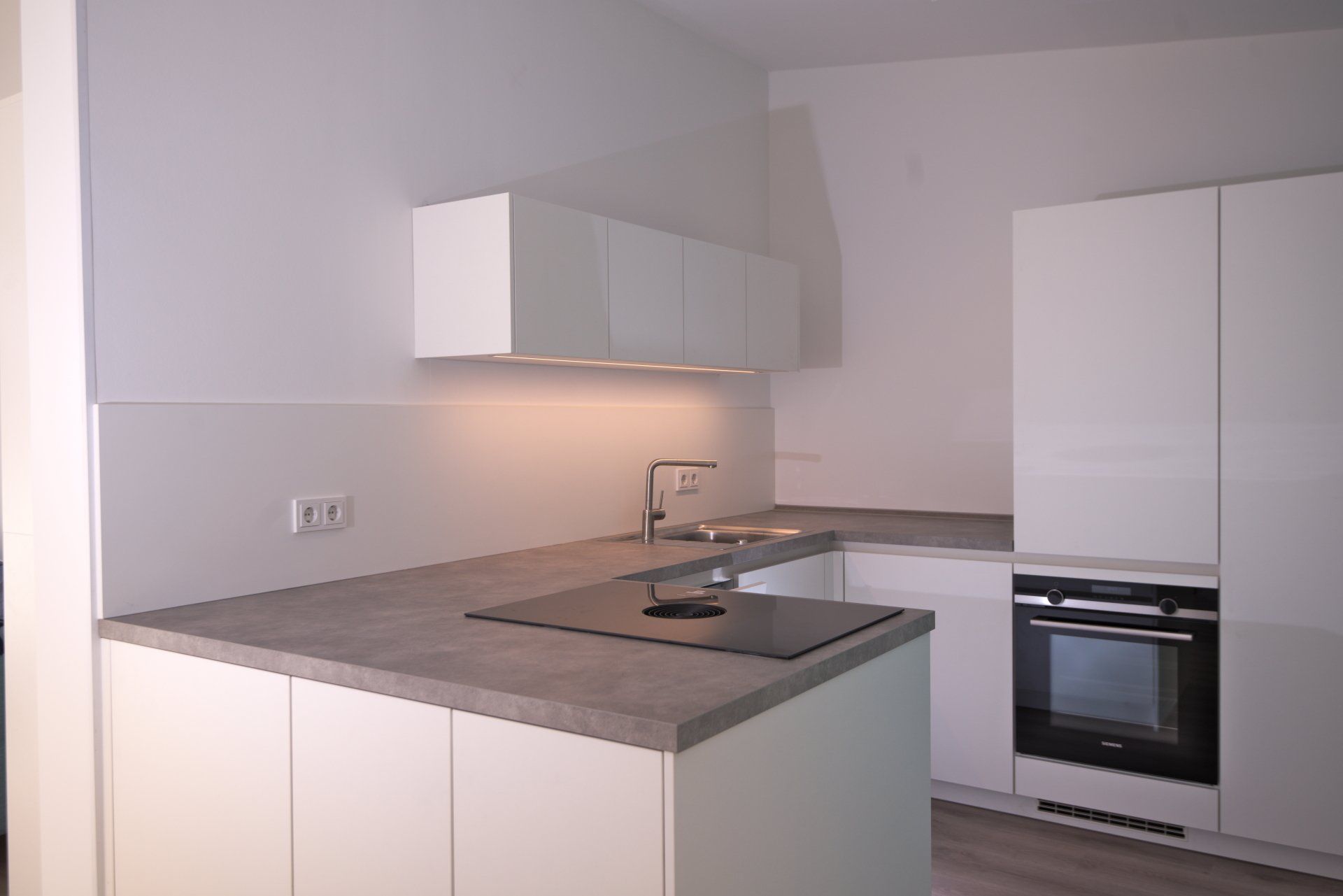 Moderne weiße Küche mit grauen Arbeitsplatten, Einbaubackofen und Wandschränken