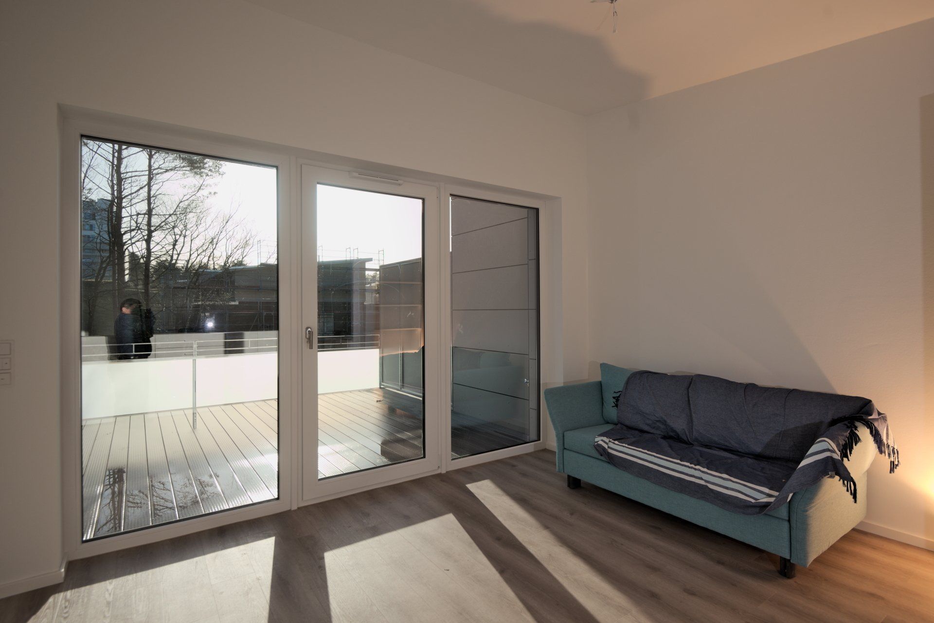Helles Wohnzimmer mit Glasschiebetüren, Holzboden und einem türkisfarbenen Sofa an der Wand.