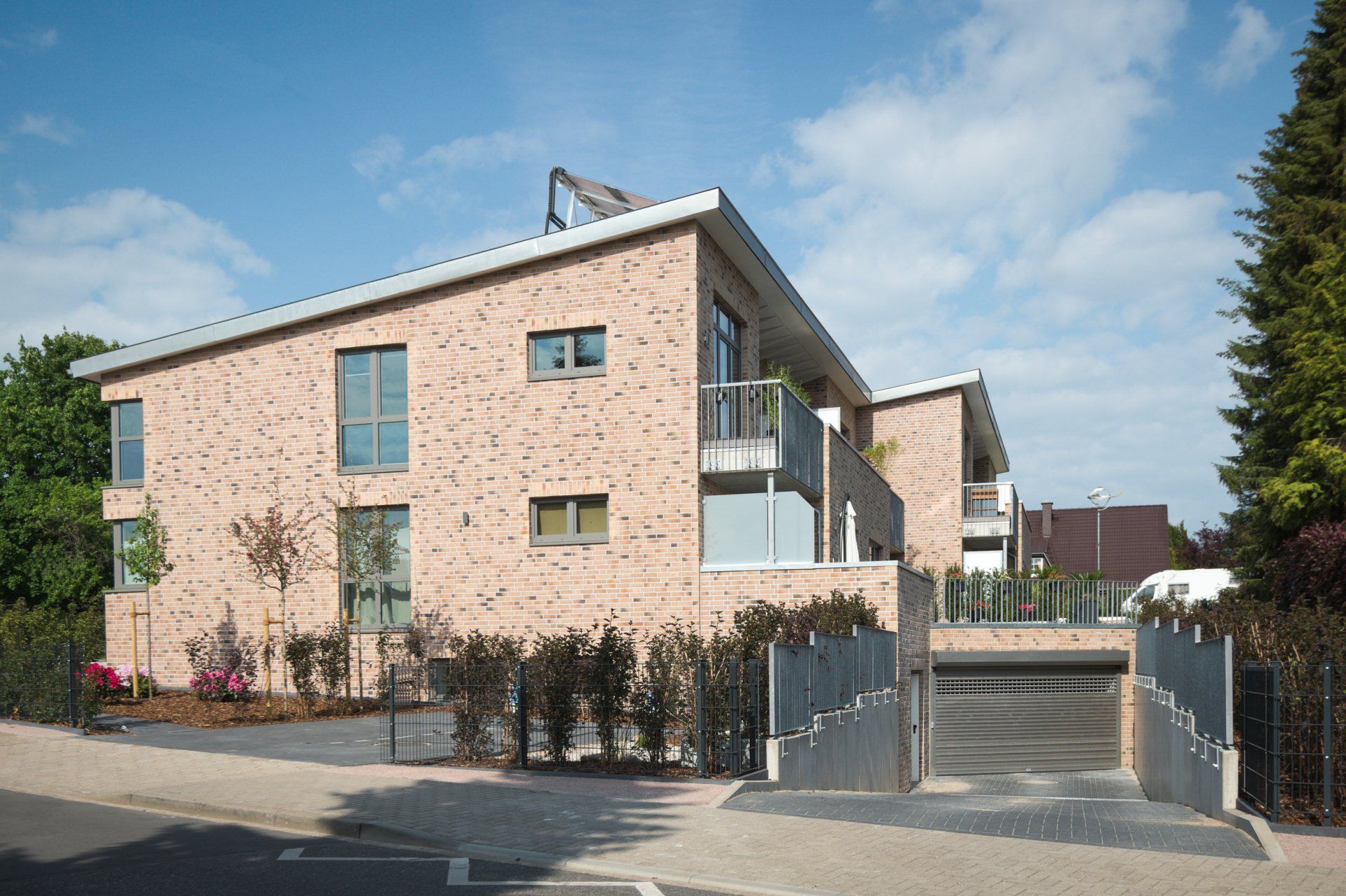 Modernes Wohnhaus mit Steinfassade, umzäuntem Eingang und Treppe unter blauem Himmel