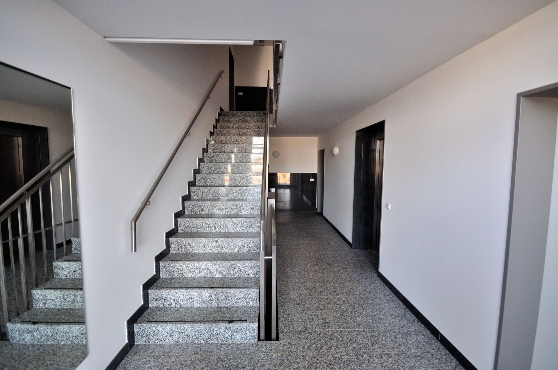Innentreppenhaus und Flur mit gemustertem Teppichboden, weißen Wänden und schwarzem Geländer.