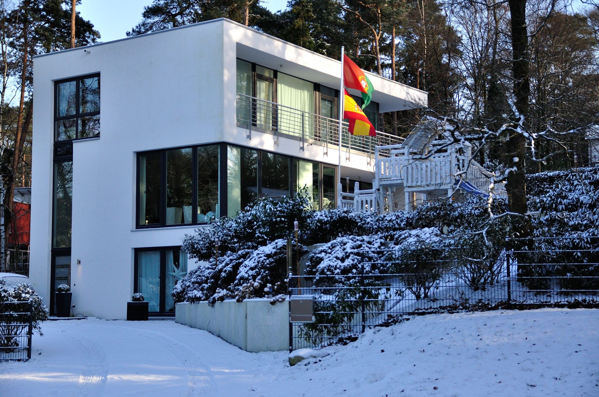 Ein schneebedecktes, modernes Gebäude mit einer Regenbogenflagge auf dem Balkon in einer bewaldeten Umgebung