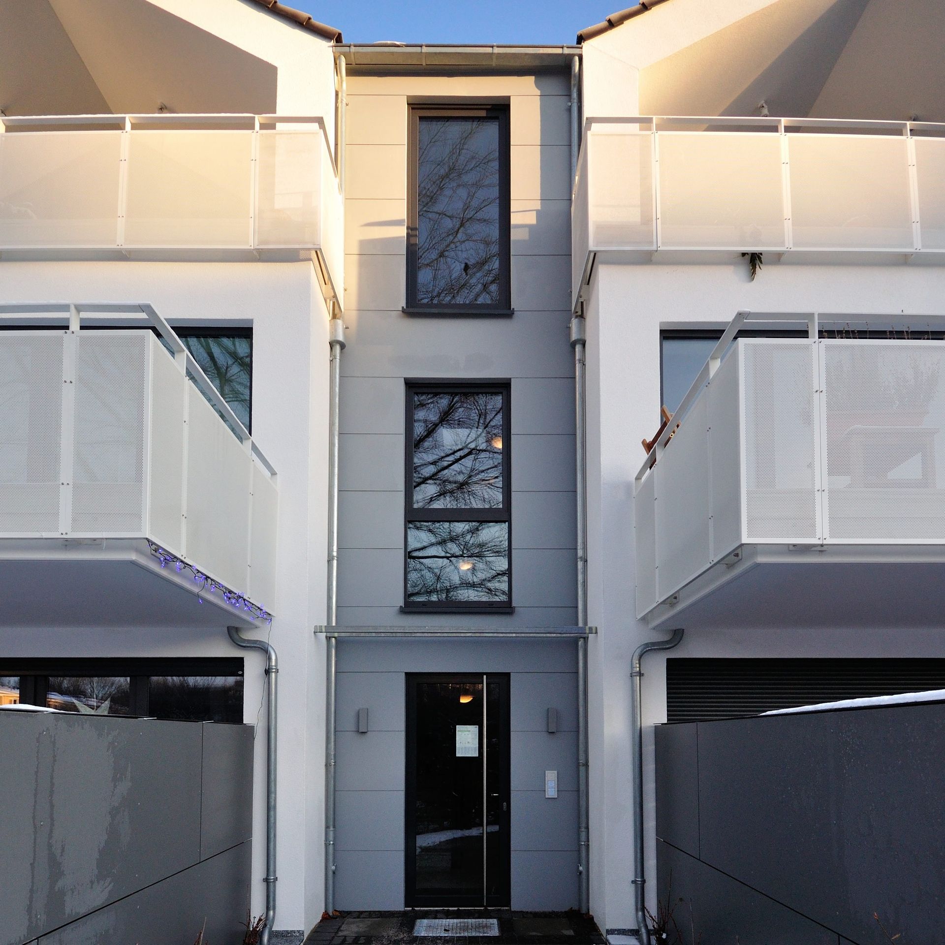 Eingang zu einem modernen Apartmentgebäude mit weißen Balkonen und zentralen, dunkel verglasten Fenstern