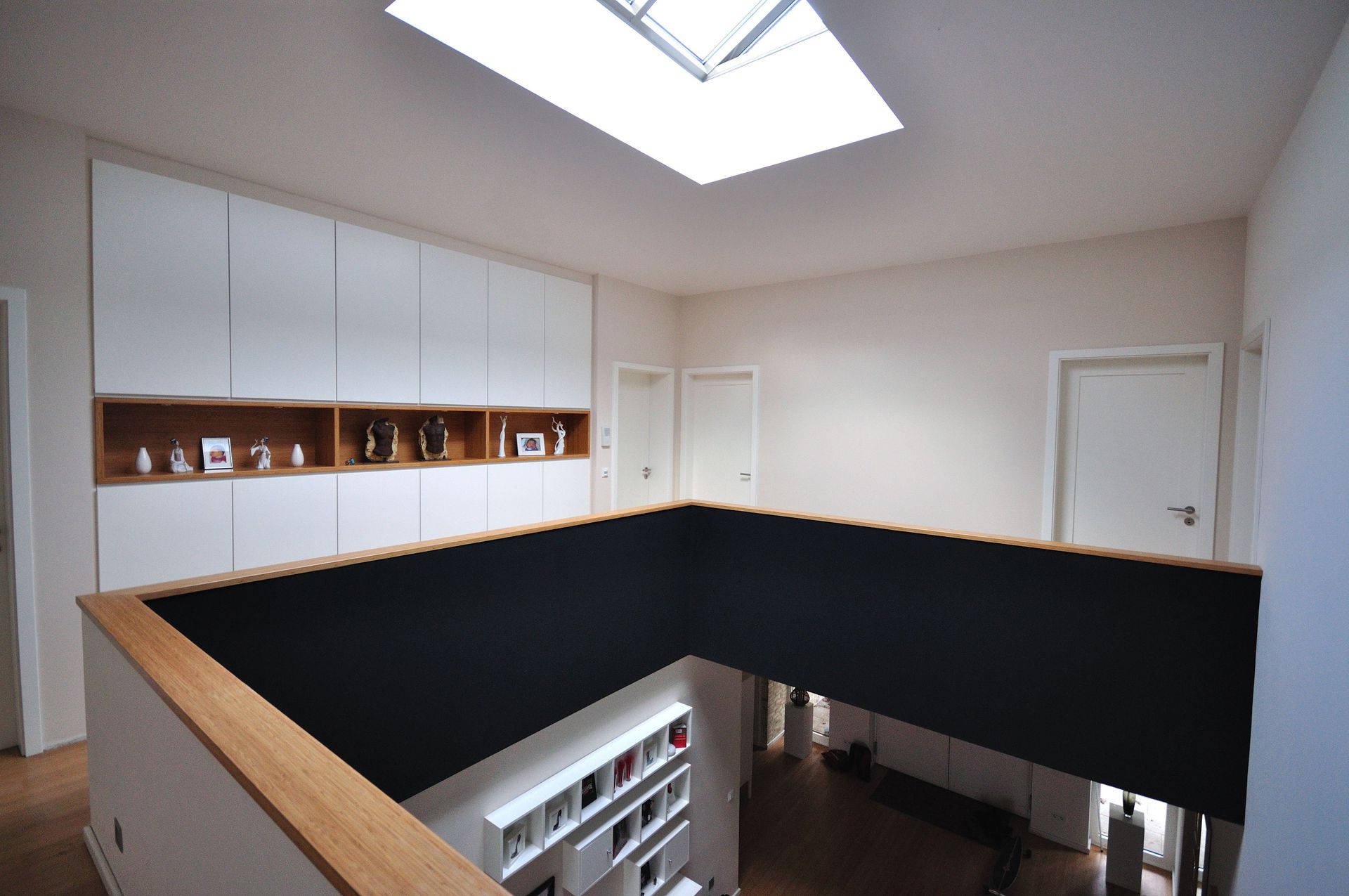 Innenbalkon mit Blick auf ein Zimmer mit weißen Wänden, Holzgeländer und Oberlicht.