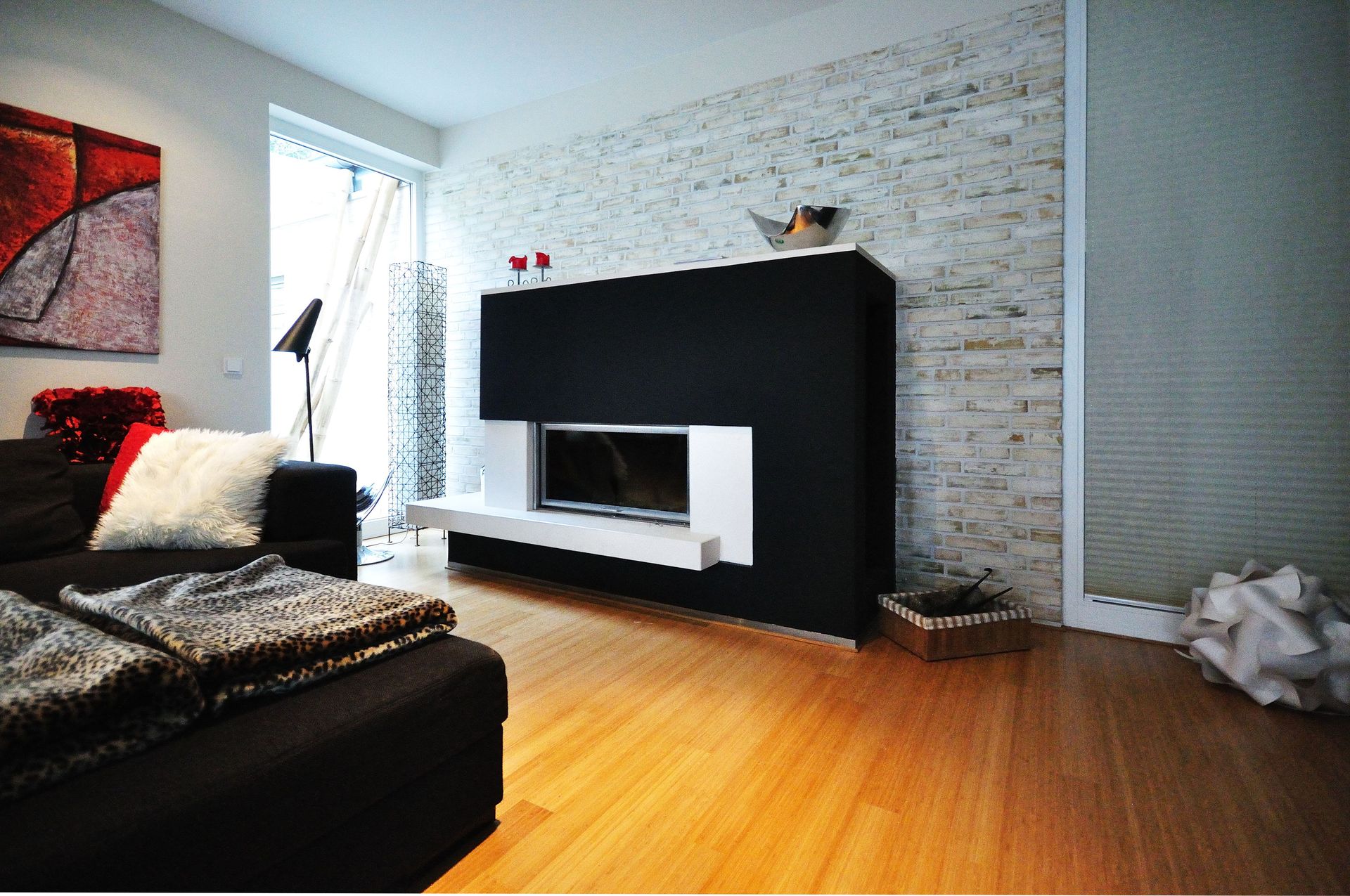 Modernes Wohnzimmer mit schwarzem Kamin, Holzboden und Sofa am Fenster