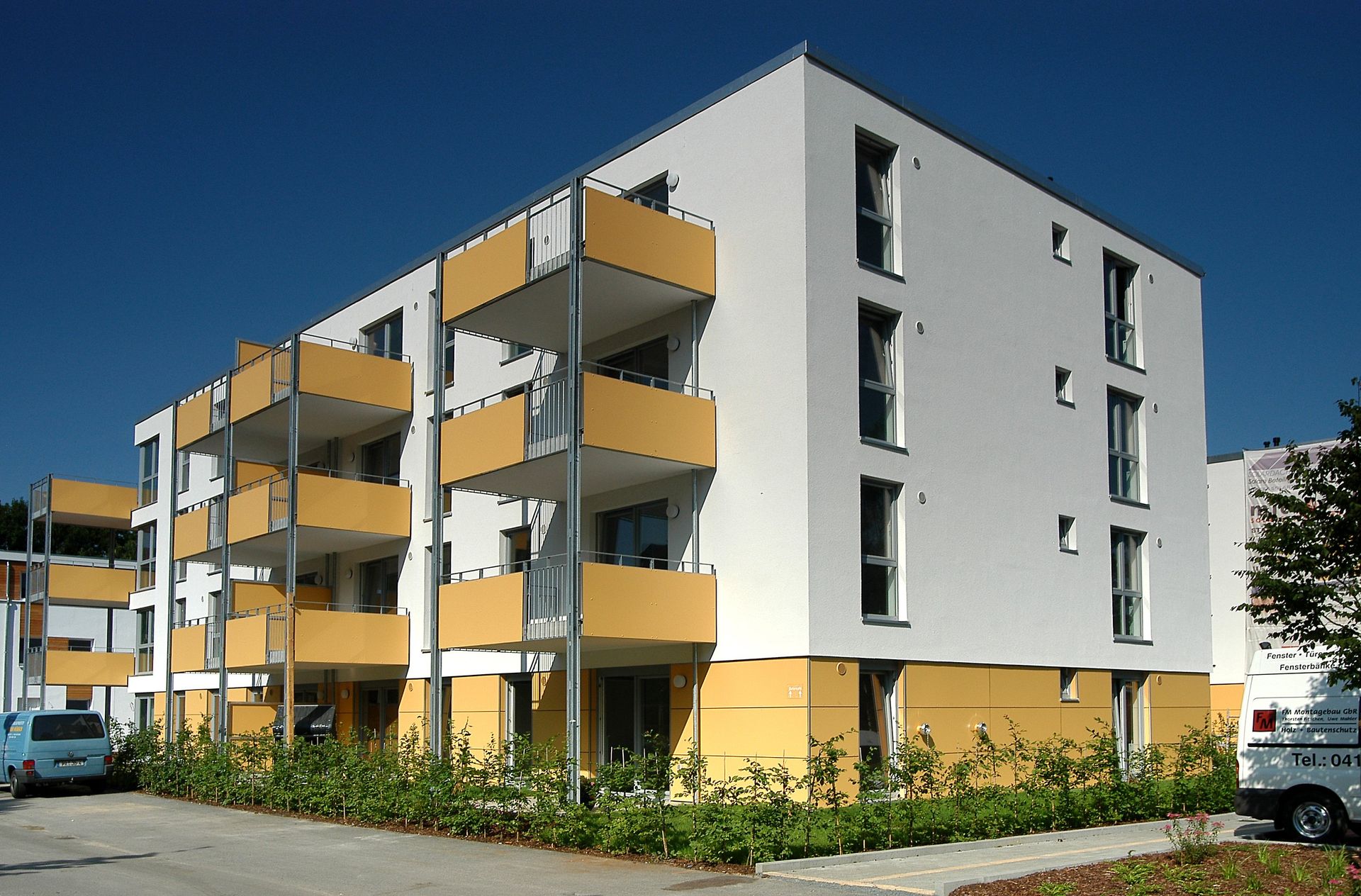 Modernes Wohnhaus mit gelben Balkonen und grauen Wänden unter blauem Himmel