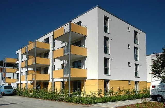 Modernes Wohnhaus mit gelben Balkonen und grauer Fassade unter blauem Himmel