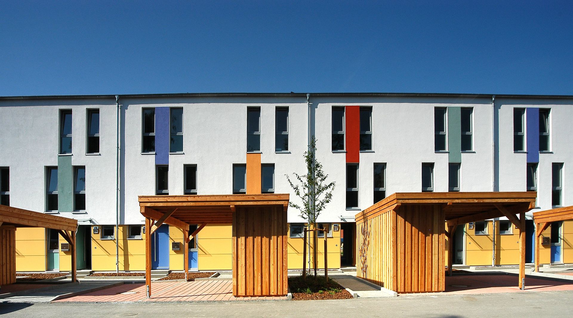 Moderne Apartmentgebäude hinter Holzbänken und Sonnenschirmen in einem sonnigen Innenhof