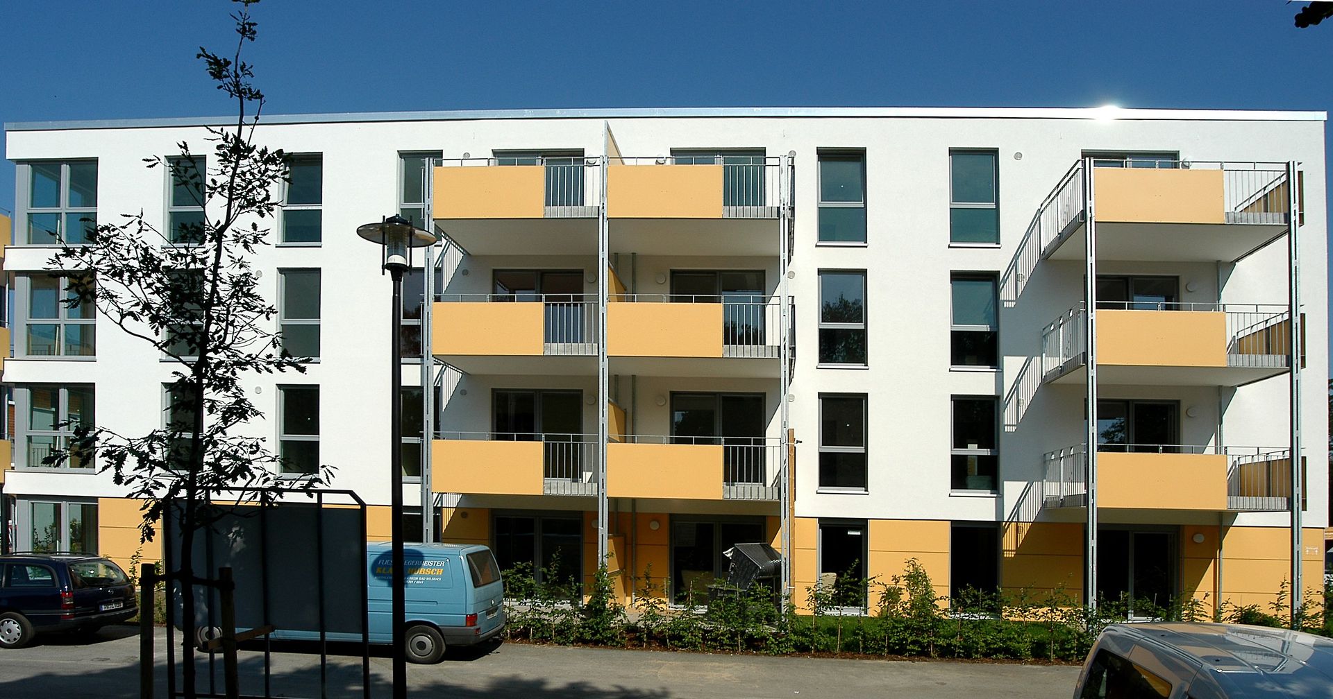 Modernes Wohnhaus mit gelben Balkonen und geparkten Autos entlang der Straße