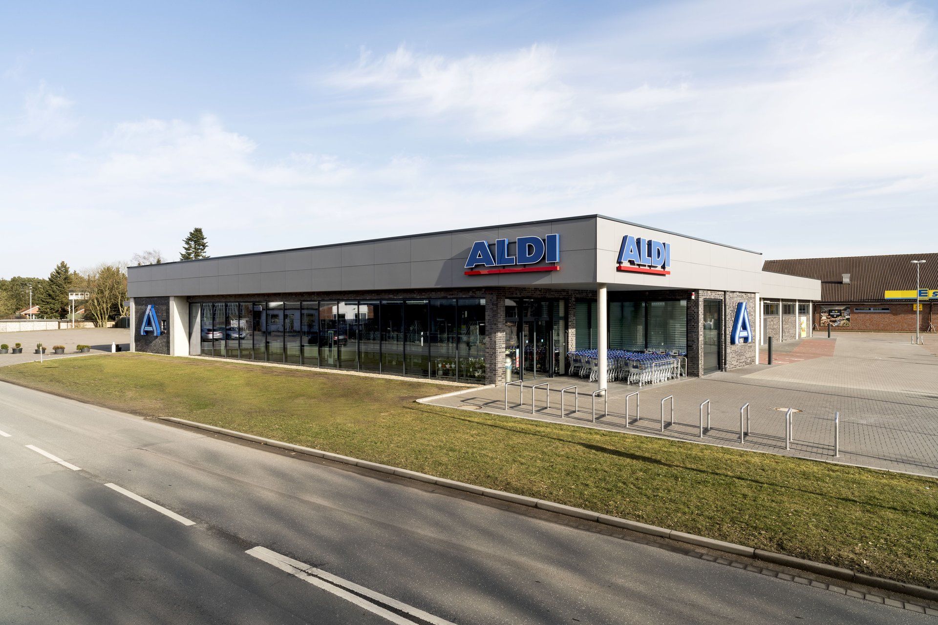 Modernes Autohausgebäude mit Glasfenstern und blau-weißer Beschilderung, neben einer leeren Straße.