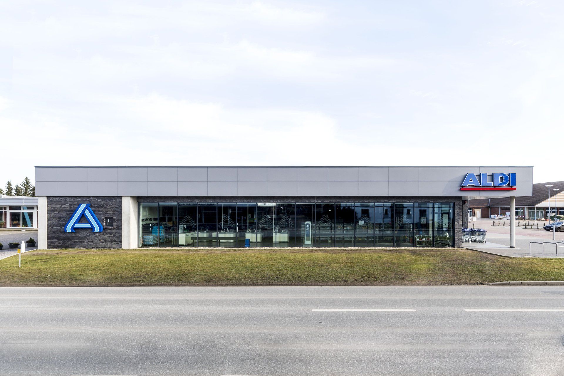 Modernes, niedriges Geschäftsgebäude mit Glasfassade und blauer Beschilderung an einer Straße.