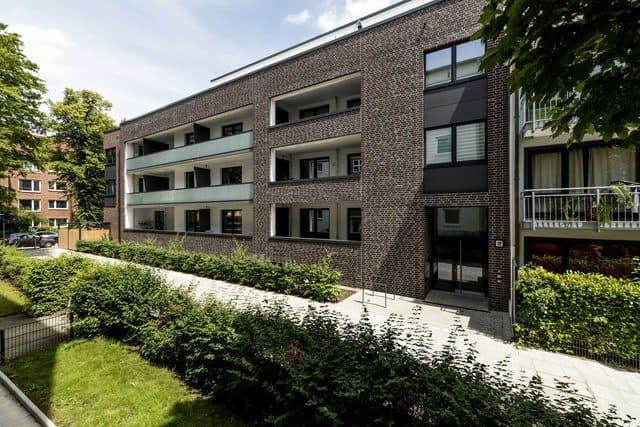 Modernes Backstein-Apartmentgebäude mit Balkonen und angelegten Grünflächen entlang eines Gehwegs
