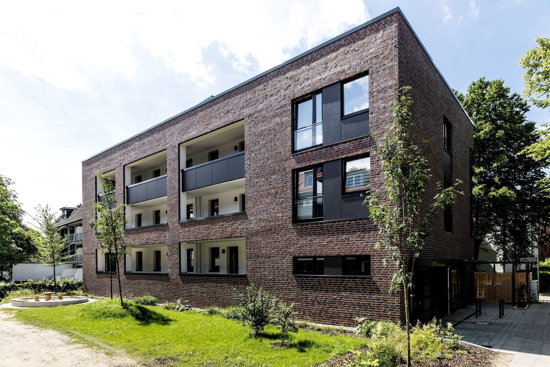 Modernes Backstein-Mehrfamilienhaus mit Balkonen und großen Fenstern an einem sonnigen Tag