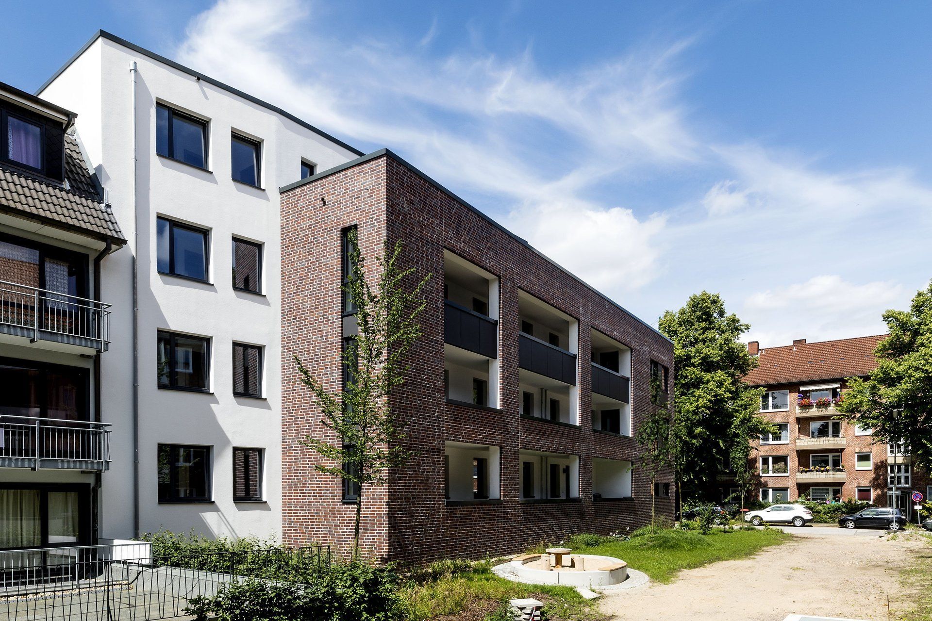 Moderne Wohngebäude mit Balkonen und einem gepflasterten Innenhof unter blauem Himmel