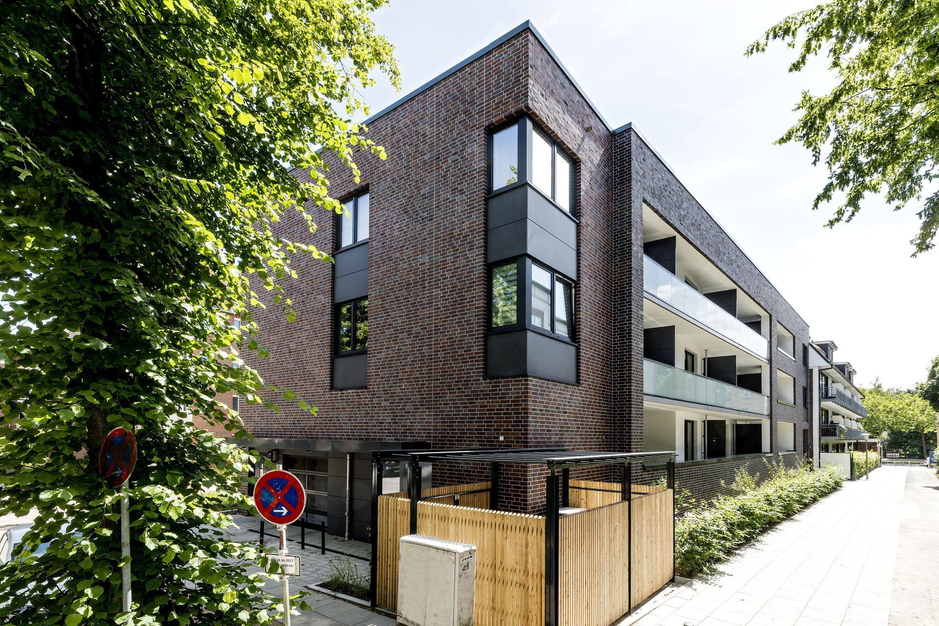 Modernes Backstein-Mehrfamilienhaus mit Balkonen an einer baumbestandenen Straße