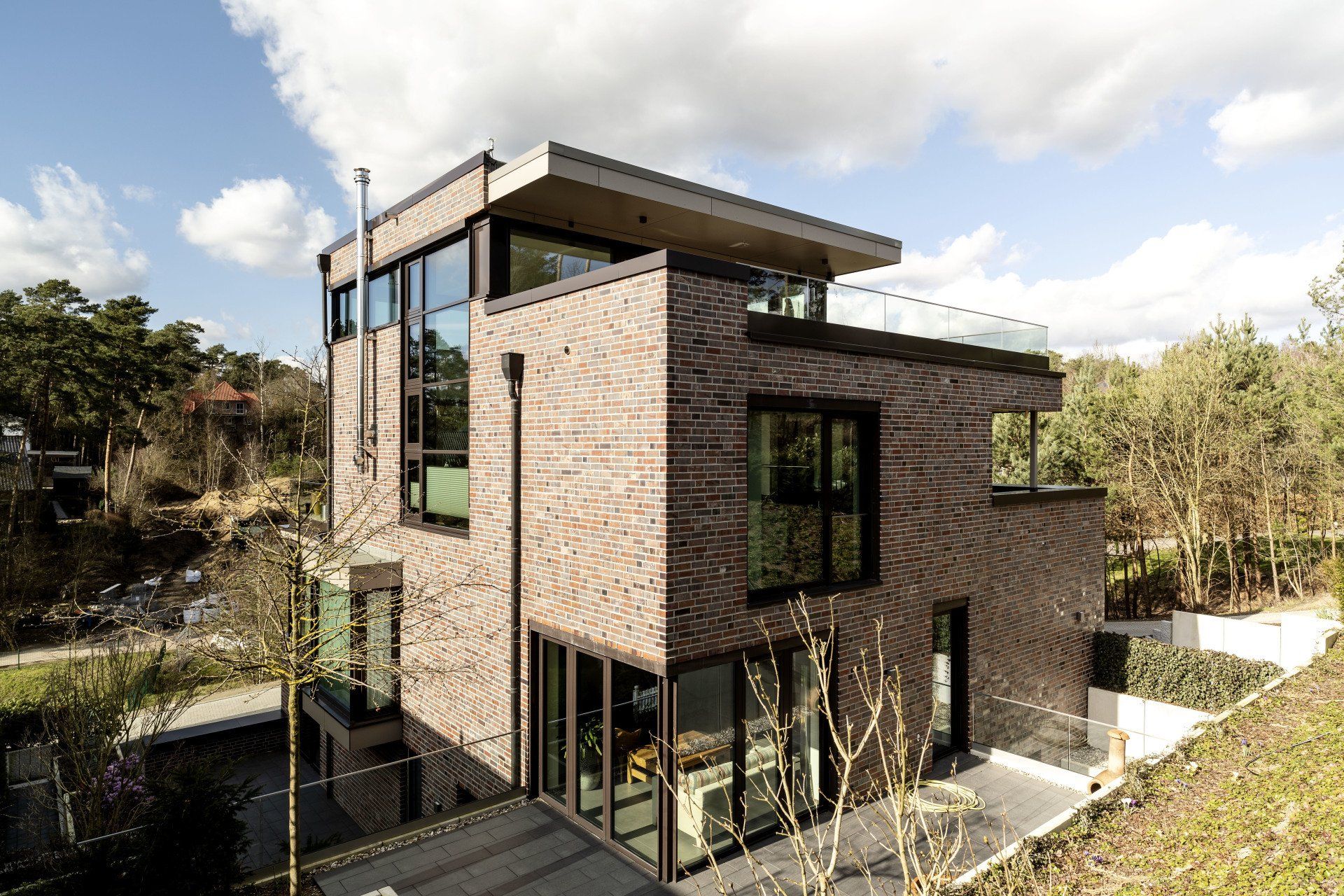 Modernes Backstein- und Glashaus mit Flachdach, großen Fenstern und umliegenden Bäumen unter einem bewölkten Himmel