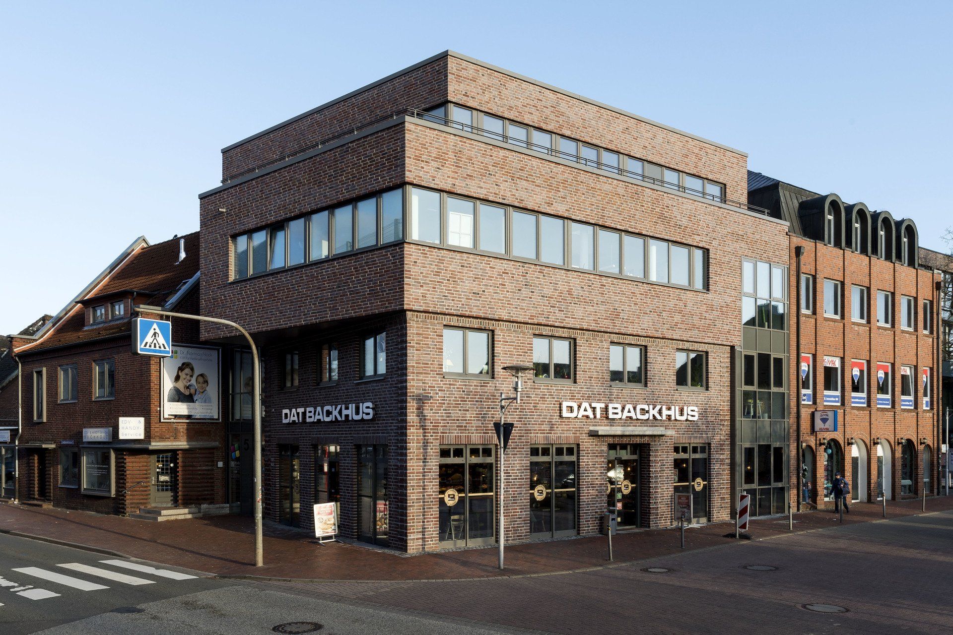 Eckgebäude aus Backstein mit großen Fenstern und einem Schaufenster mit der Aufschrift „DAG SUSHI“ an einer Straßenecke.