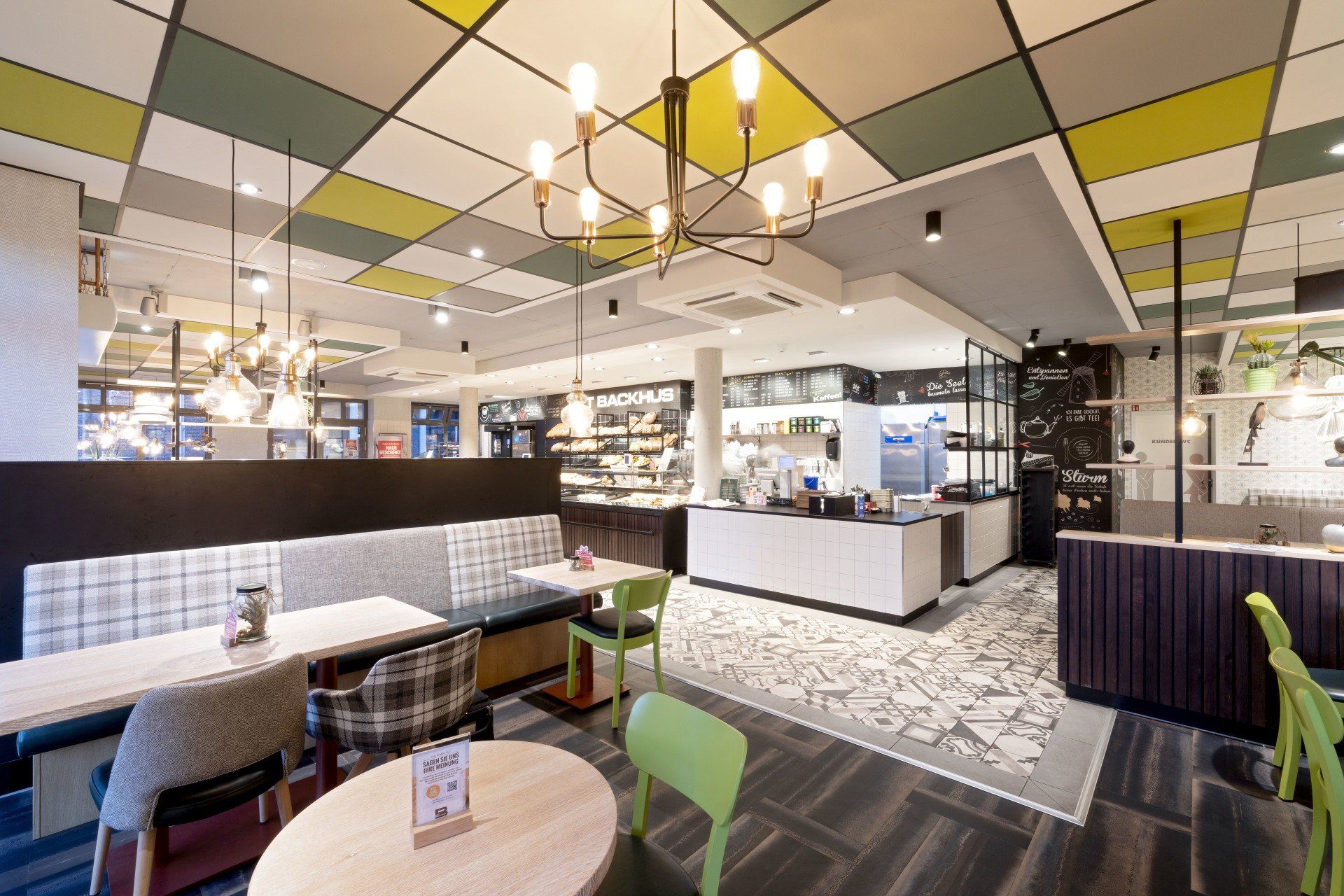 Helles, modernes Café-Interieur mit farbenfrohen Deckenpaneelen, Sitzgelegenheiten und Thekenbereich