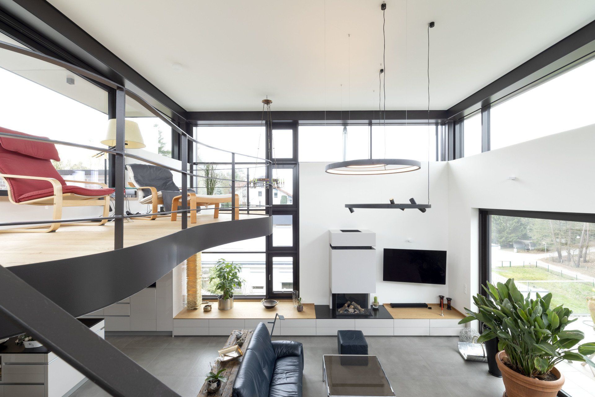 Modernes Loft-Wohnzimmer mit großen Fenstern, schwarzer Treppe, weißen Wänden und Zimmerpflanzen