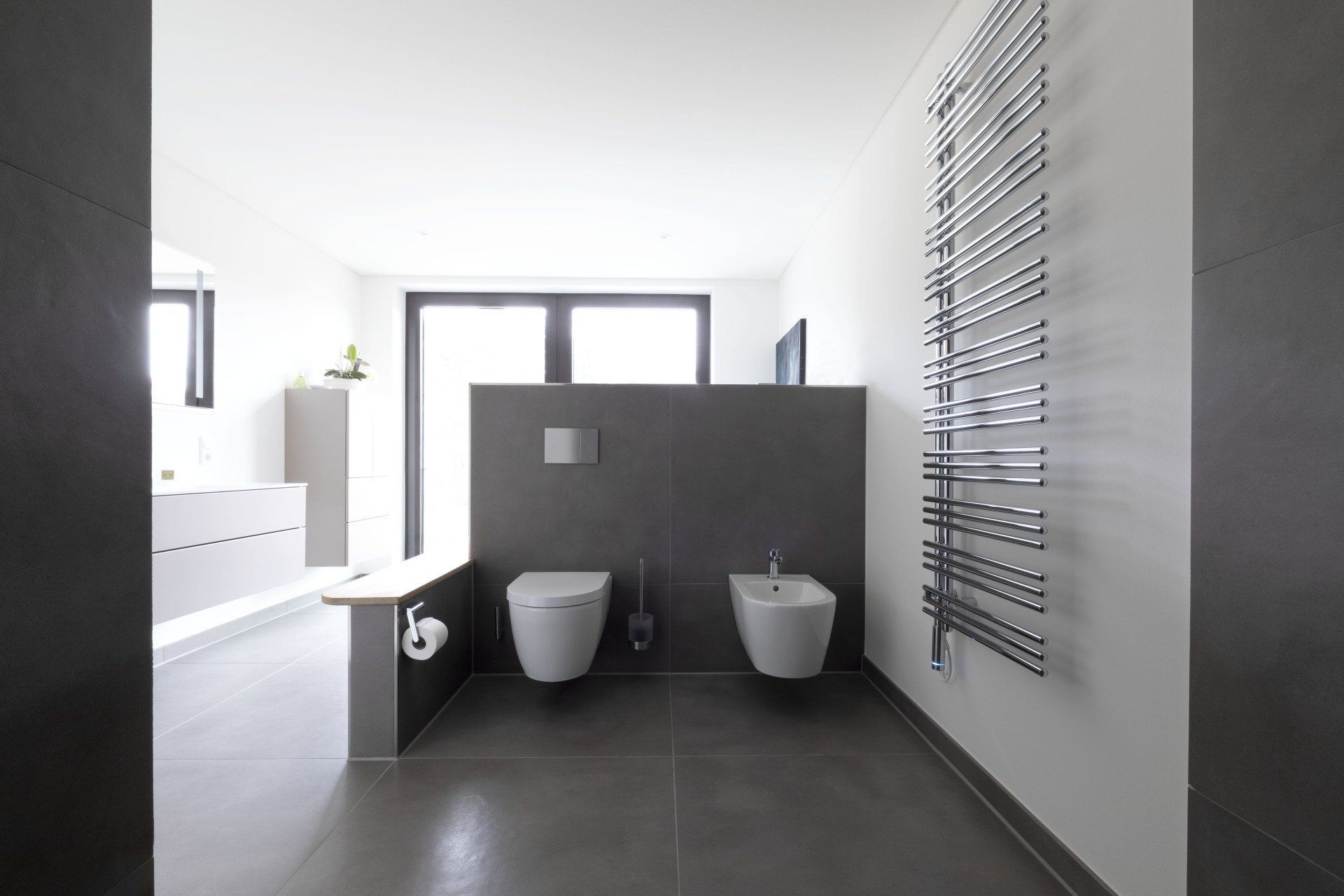 Modernes, minimalistisches Badezimmer mit zwei wandmontierten Waschbecken, weißen Armaturen und einer dunklen Akzentwand