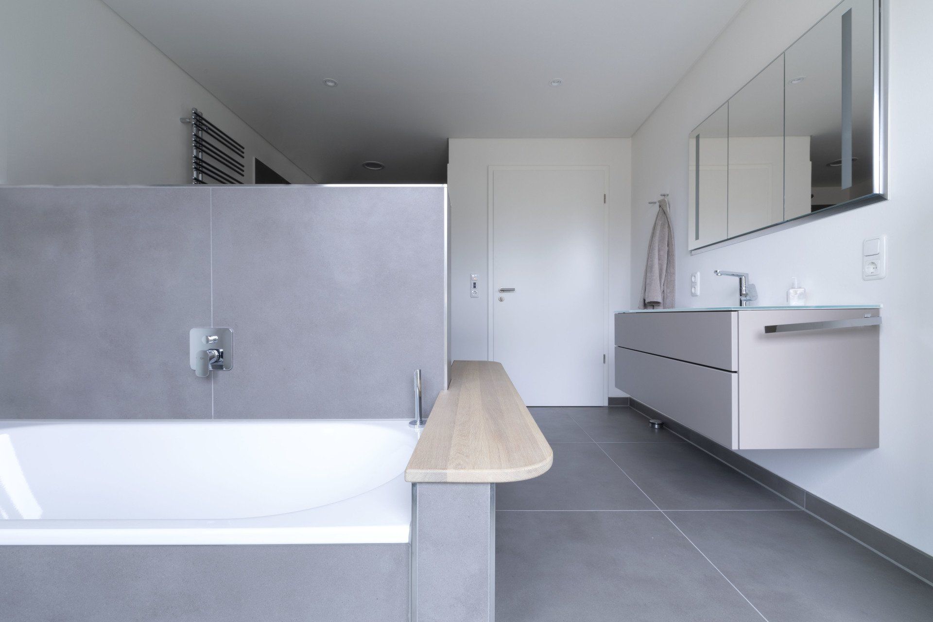 Modernes Badezimmer mit freistehender Badewanne, grauen Fliesen, Holzelementen und schwebendem Waschtisch.