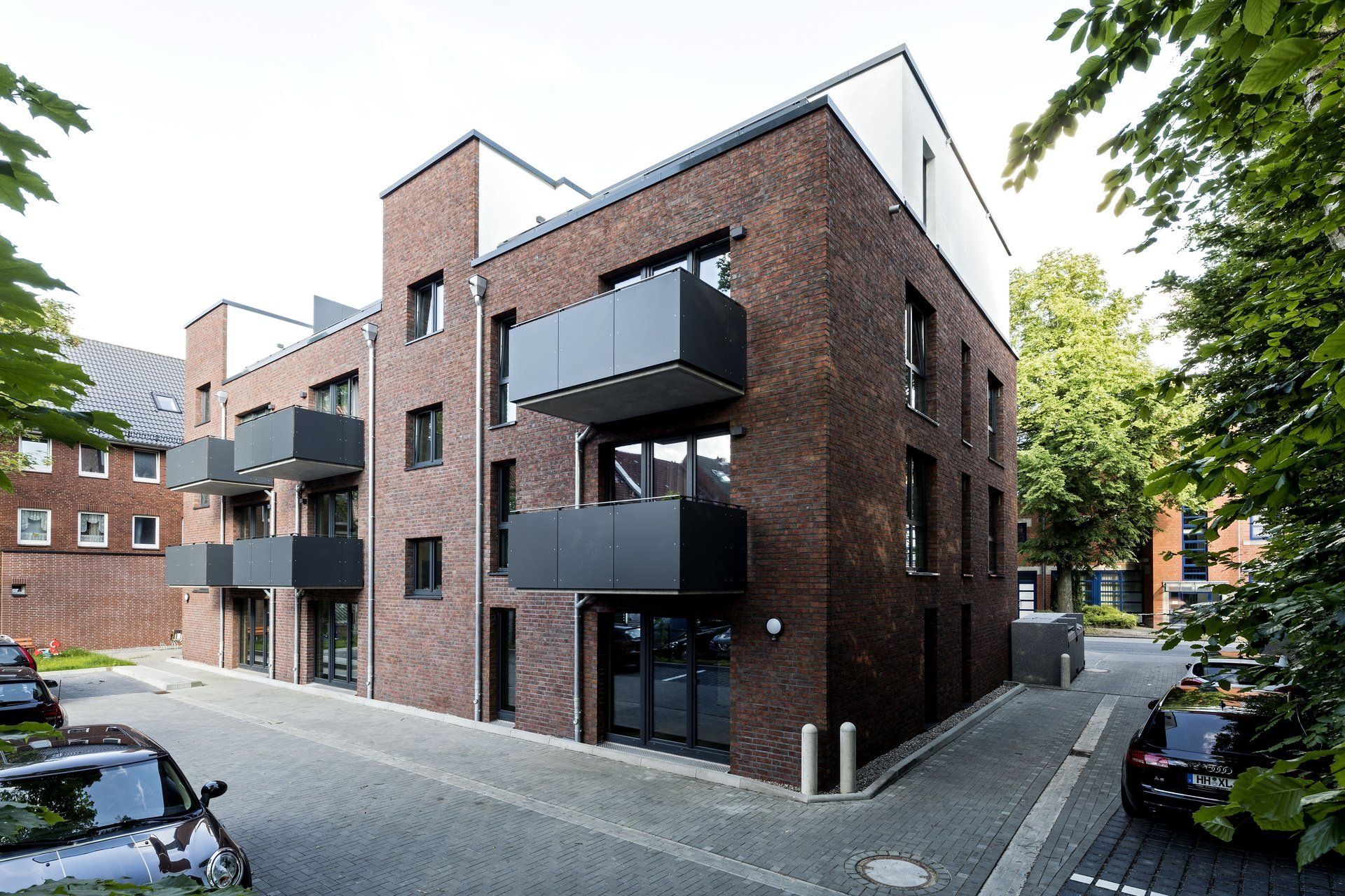 Modernes Backstein-Mehrfamilienhaus mit Balkonen in einer ruhigen Straße, von der Ecke aus gesehen