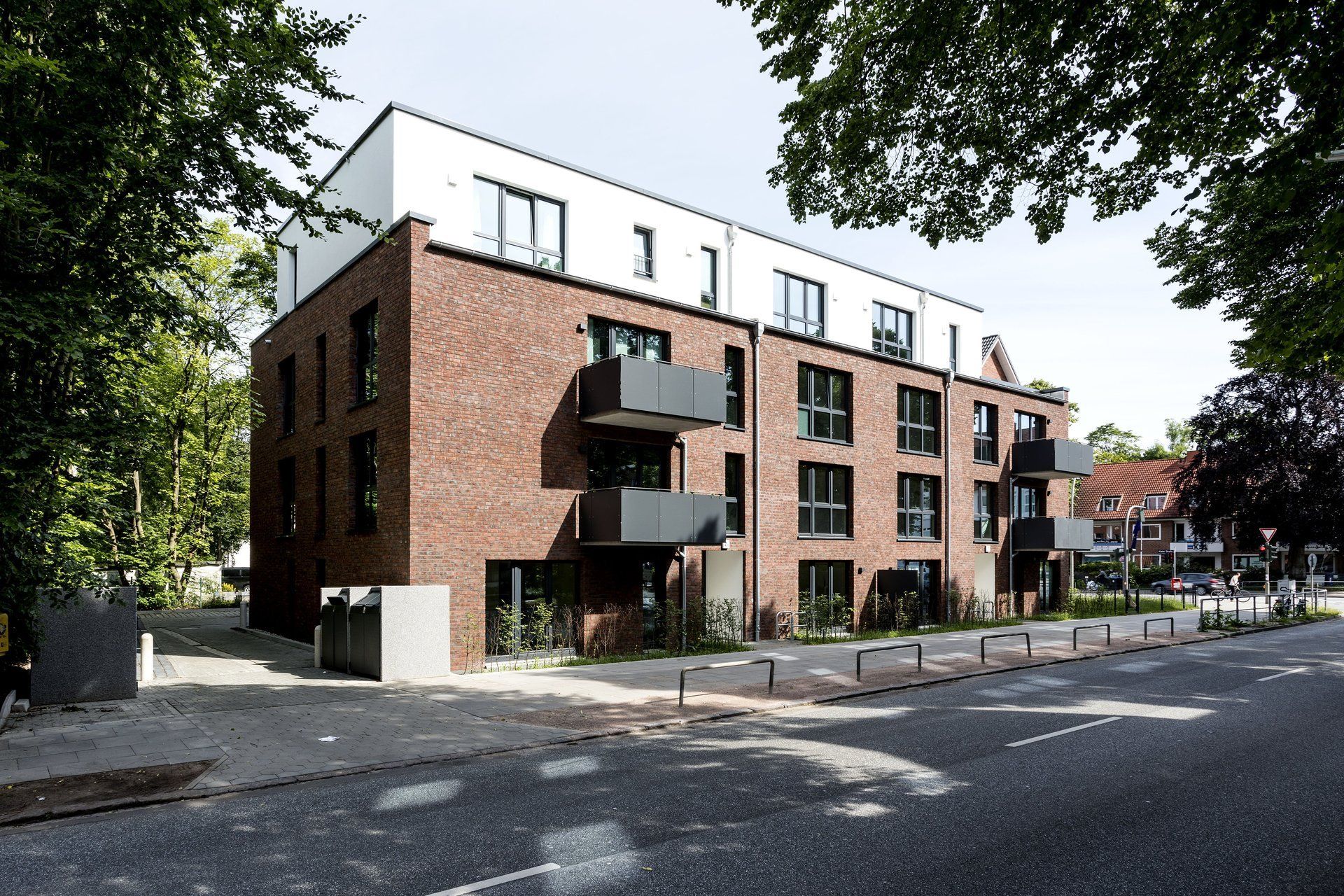 Modernes Backstein-Mehrfamilienhaus mit Balkonen an einer baumbestandenen Straße