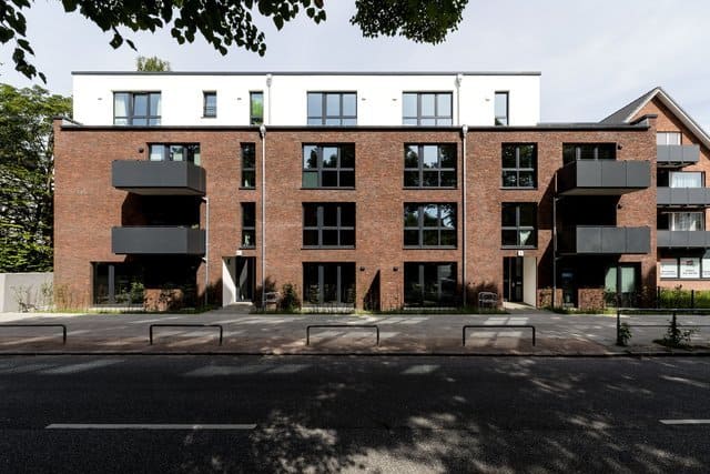 Modernes Backstein-Mehrfamilienhaus mit Balkonen und Dachterrasse, von der Straße aus gesehen.