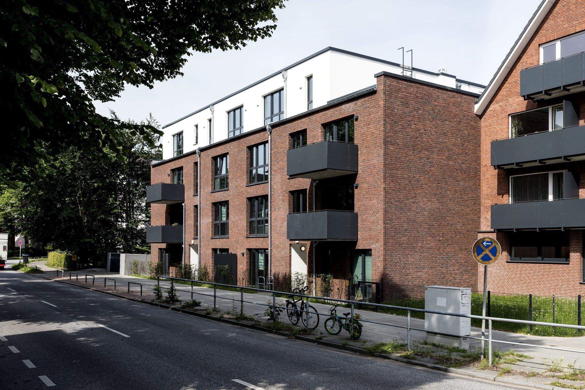 Moderne Backstein-Apartmentgebäude entlang einer von Bäumen gesäumten Straße mit Balkonen und abgestellten Fahrrädern.