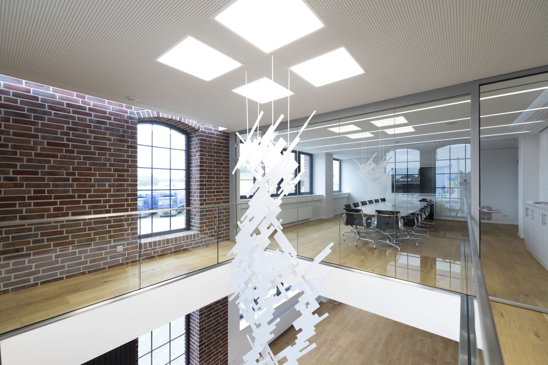 Moderne Bürolobby mit Glaswänden, Backsteinelementen und einer weißen Hängeskulptur unter Oberlichtern.