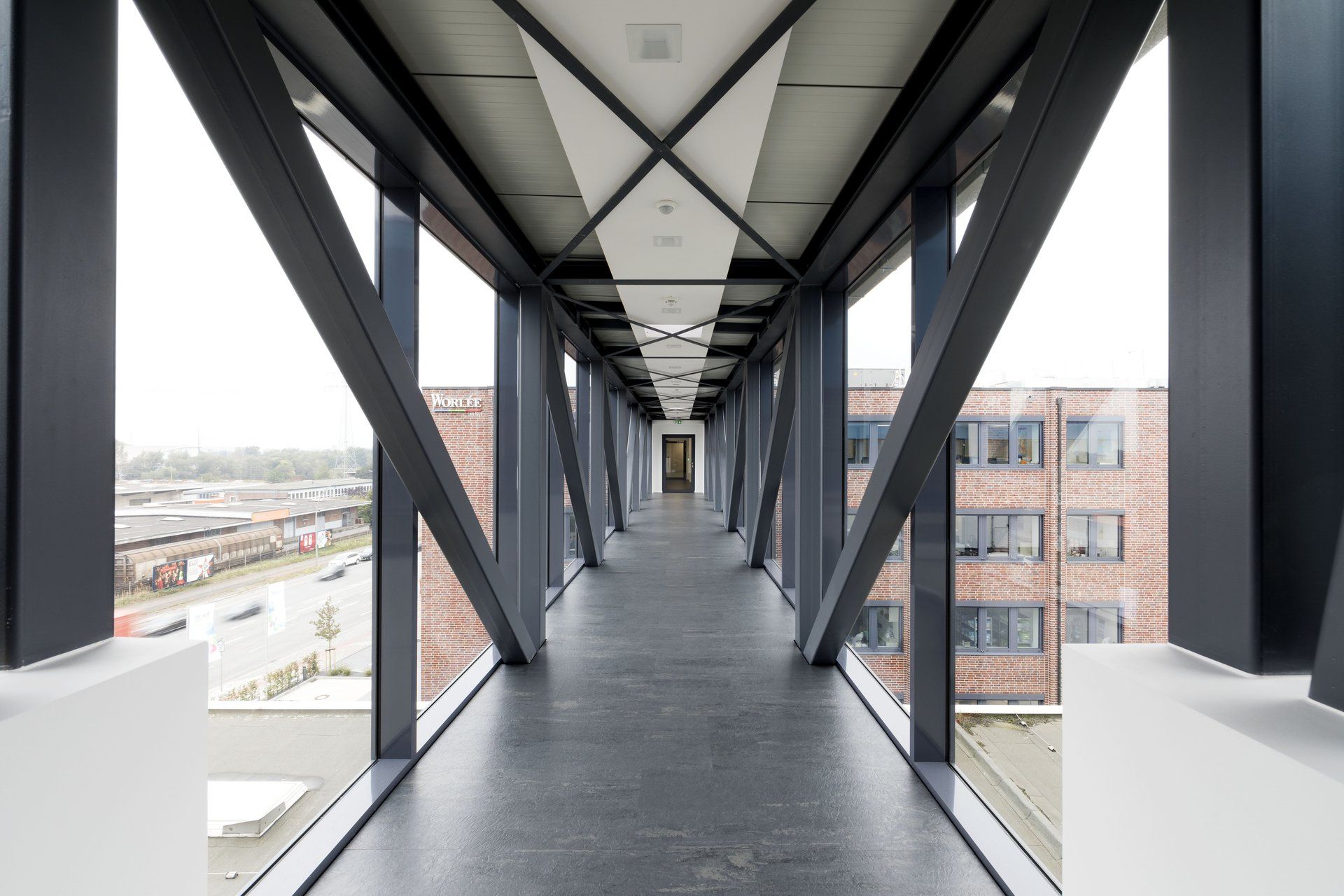 Moderner gläserner Skybridge-Korridor mit diagonalen Stahlträgern und Blick auf die Stadt durch die Fenster