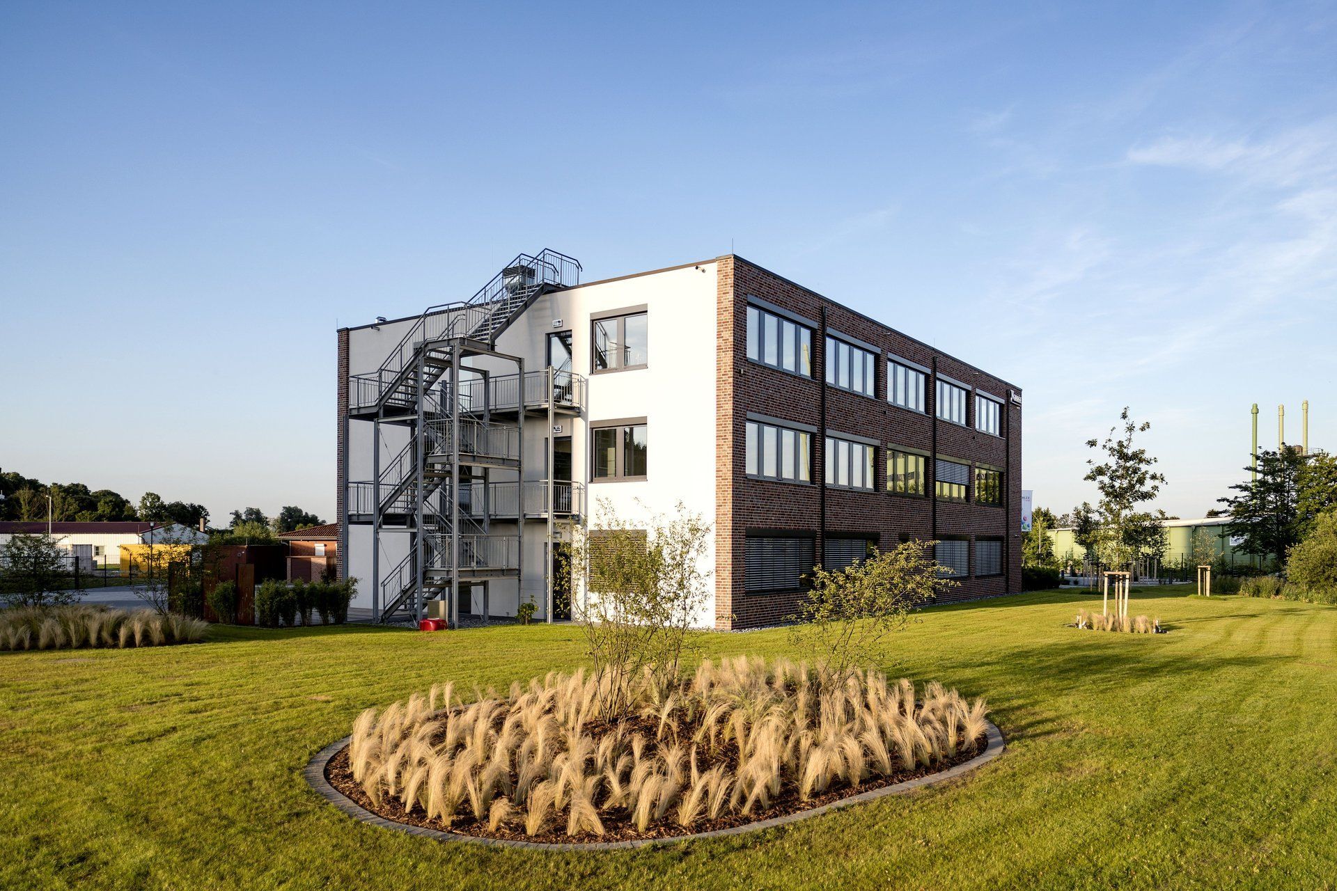 Modernes Bürogebäude neben einer grünen Wiese unter klarem, blauem Himmel